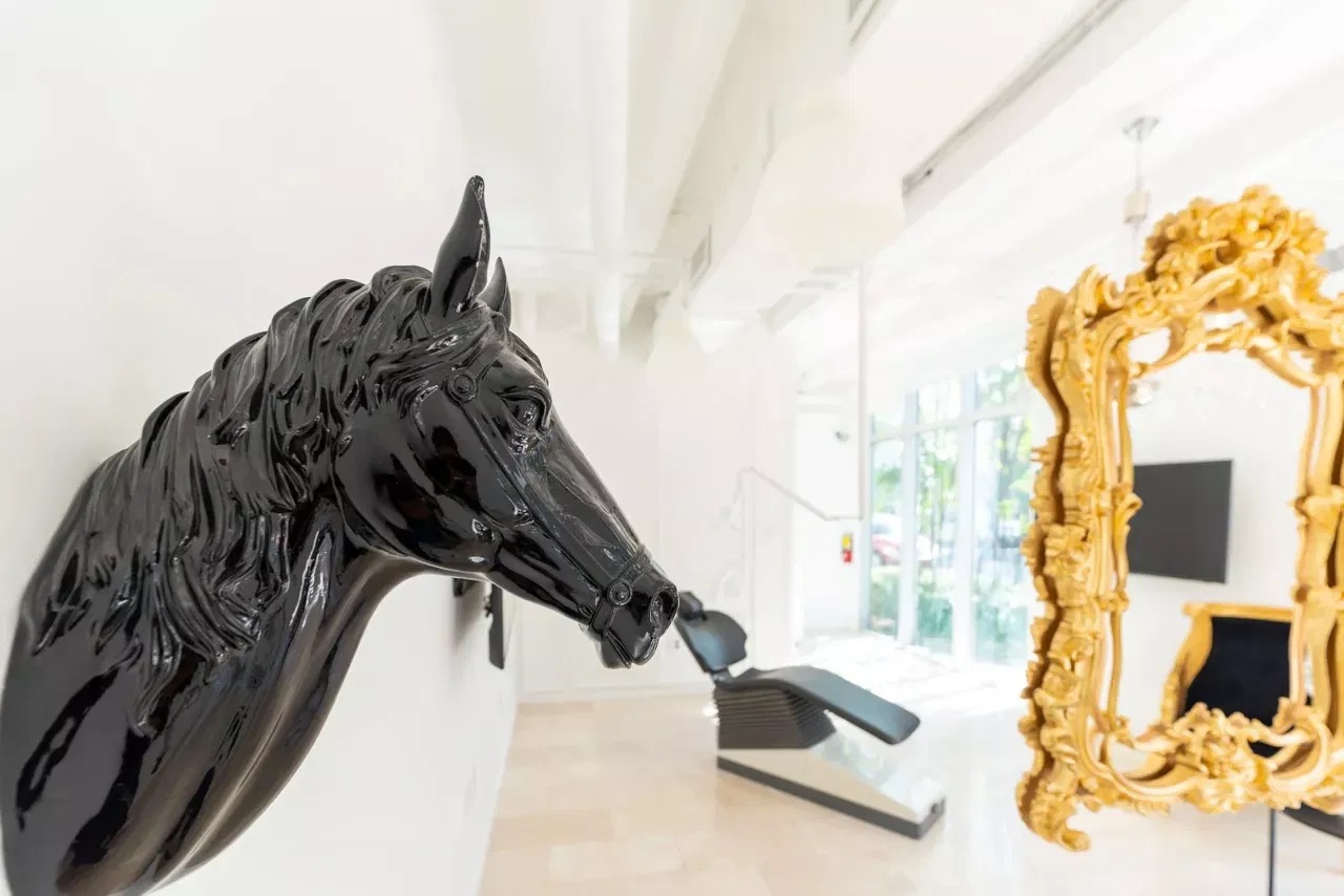 The image shows two black horse sculptures with golden accents placed on either side of a large gold mirror, set against an interior wall with a modern design aesthetic.