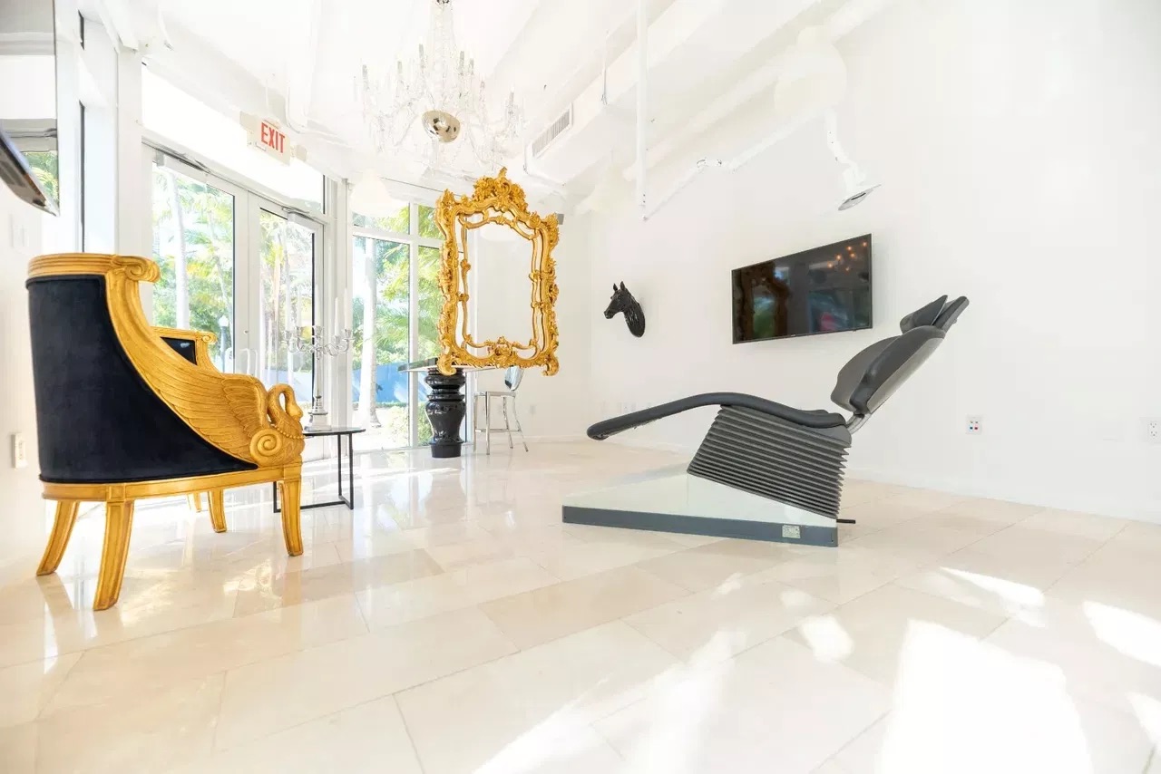 The image shows a luxurious interior space with a modern design featuring high-end furniture, large windows allowing natural light to flood the room, and a sophisticated color scheme.