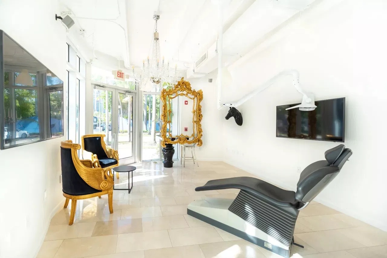 The image shows an interior space with a modern design, featuring a salon-like setting with stylish furniture, a large mirror, and various decorative elements.