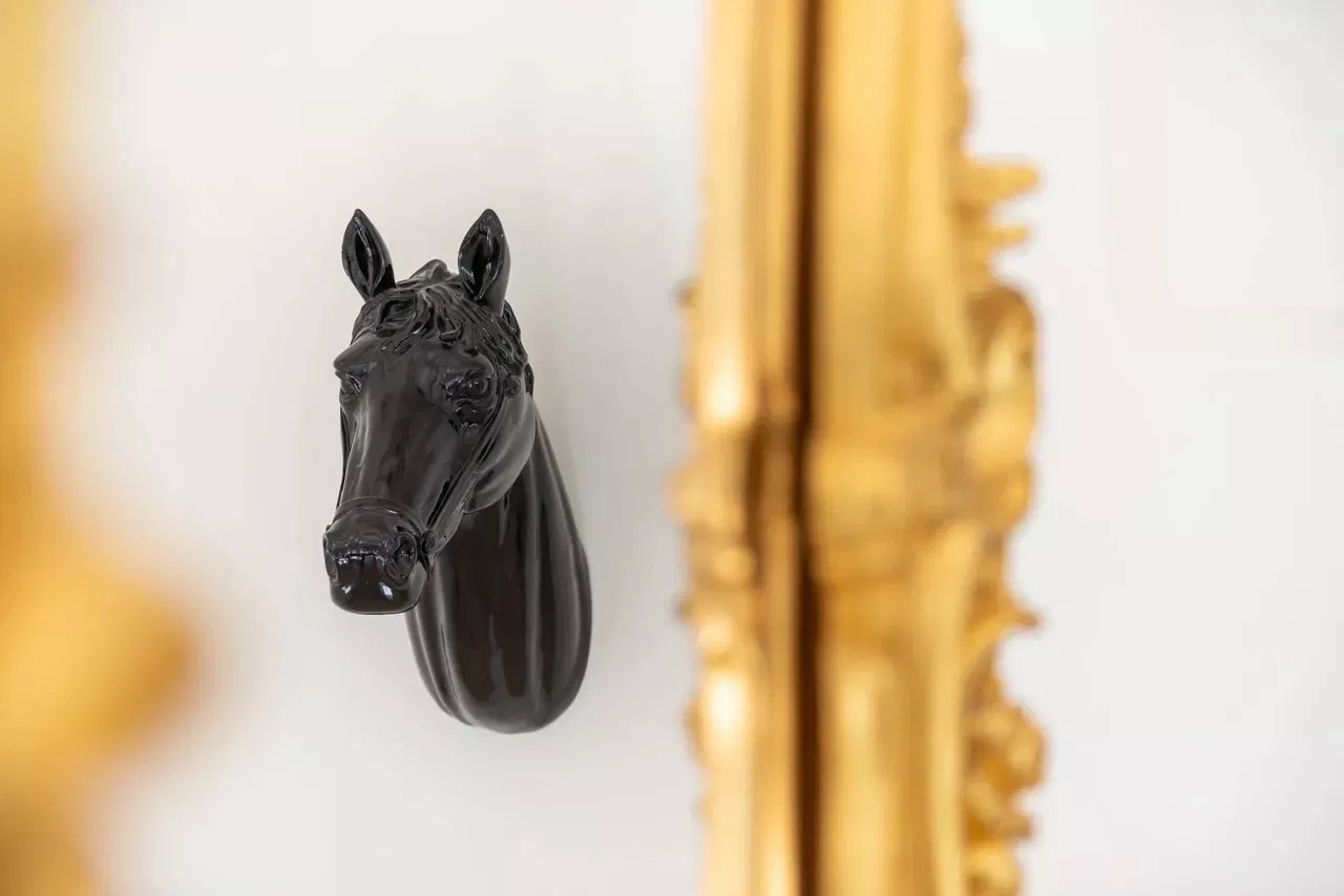 The image shows a black horse figurine mounted on a wall above a gold-framed mirror.