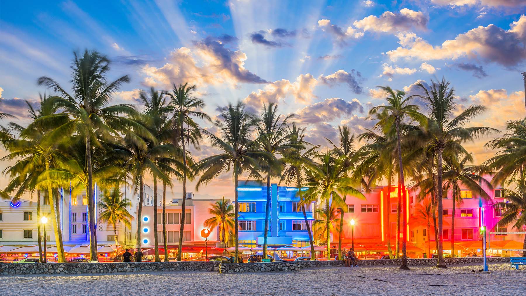 The image depicts a beach scene at sunset with palm trees and colorful lights illuminating the area.