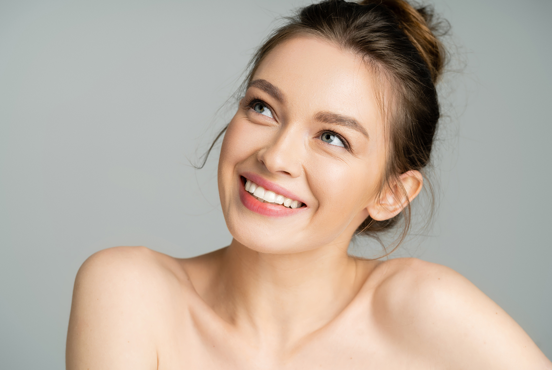 A smiling woman with light skin, wearing makeup and a necklace, against a neutral background.