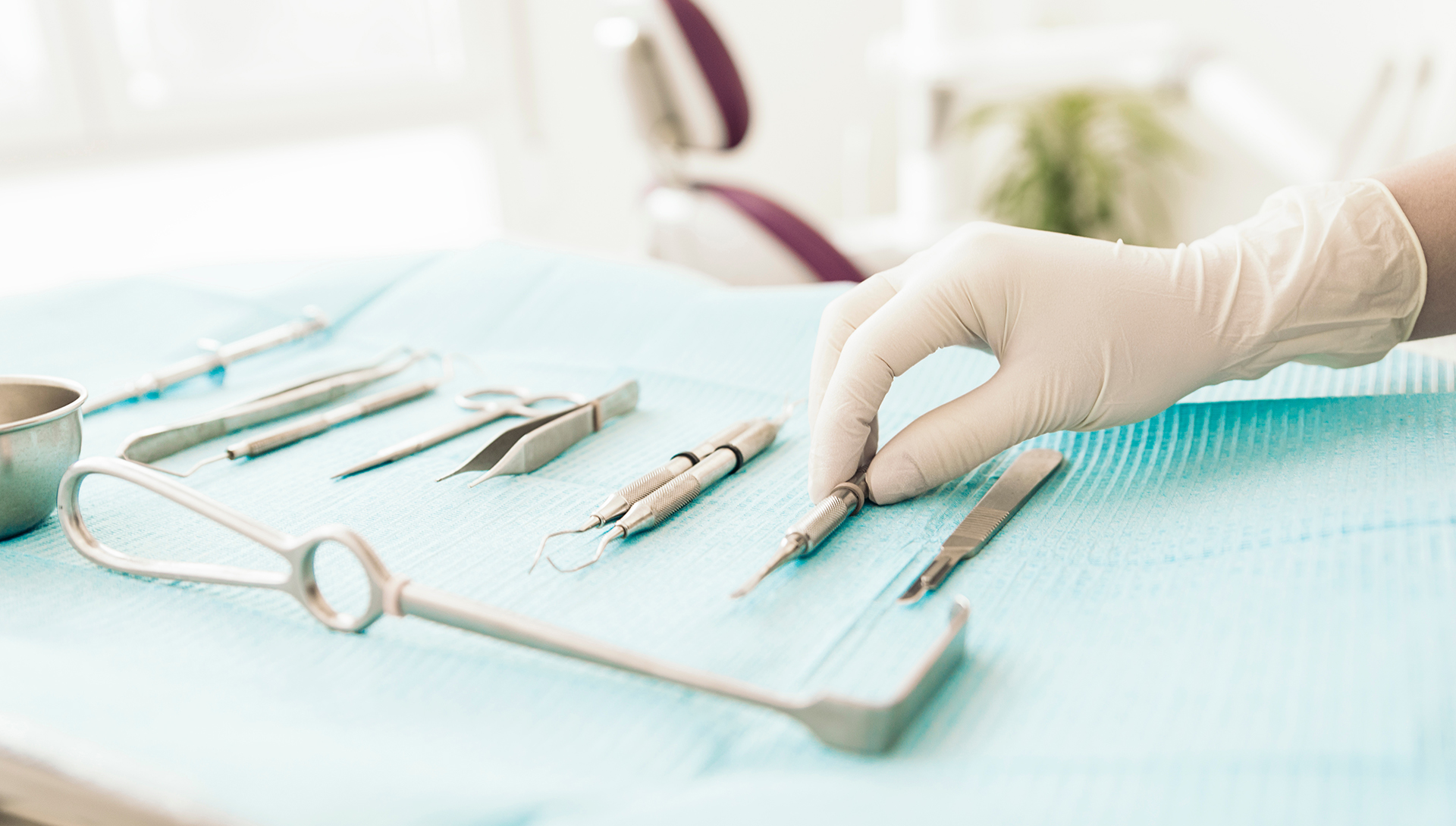 The image depicts a close-up view of surgical instruments and equipment, including scissors and tweezers, on a blue cloth surface, with a person s hand wearing gloves holding one of the tools.