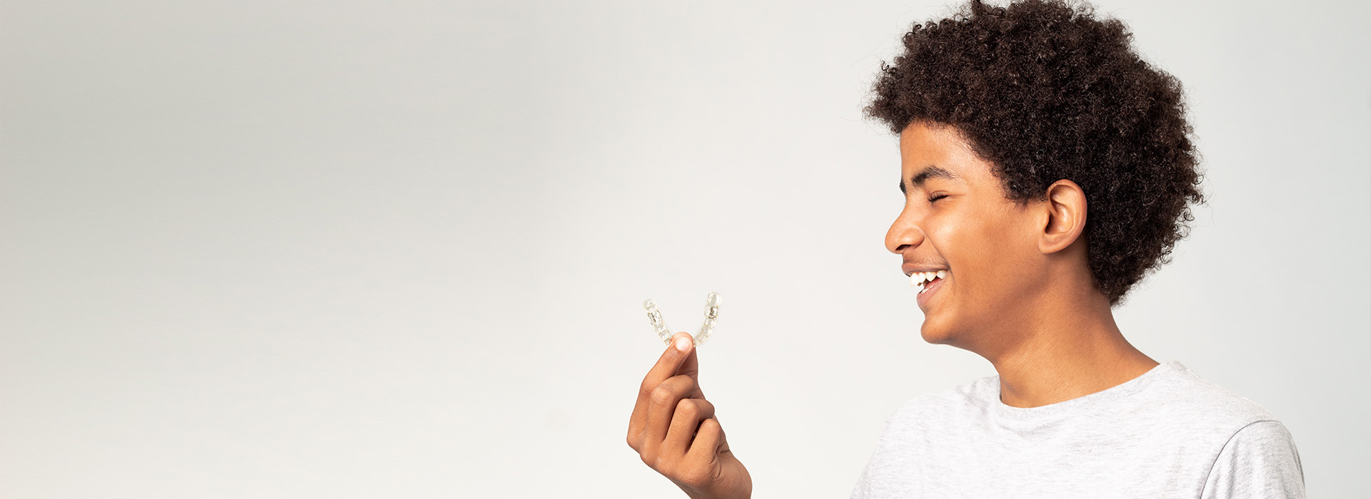 A young individual with a joyful expression, holding a small plant, set against a blurred background.