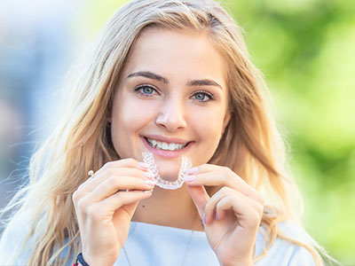 Smiling woman holding a toothbrush with a smiley face on it.