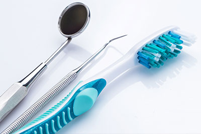 A collection of dental tools, including a toothbrush with blue bristles and a silver dental mirror, arranged on a white surface.
