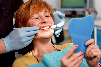 A woman sitting in a dental chair, smiling broadly, with a hygienist applying a blue mouthguard to her teeth.