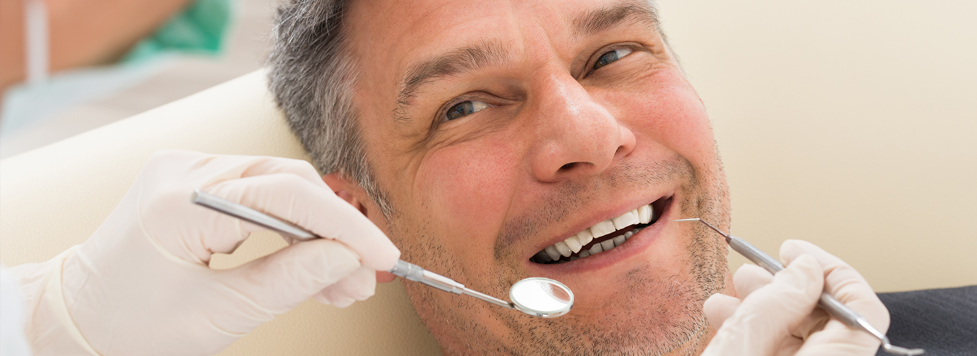 A man in a dental chair receiving a dental procedure, with a smiling expression and a dental professional working on his teeth.