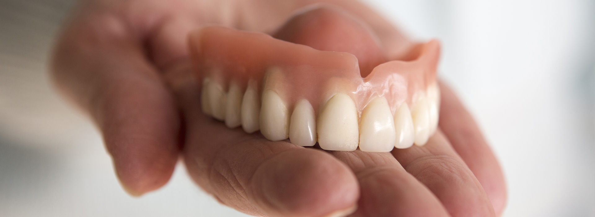 The image shows a person s hand holding an upper denture with artificial teeth.