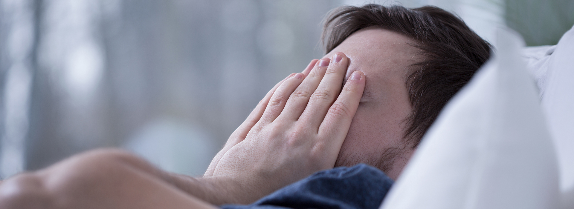 A person with their face covered by their hands, lying on a bed.