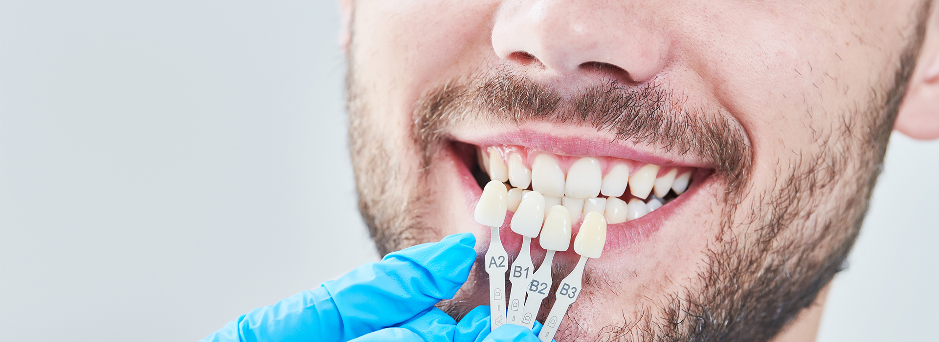 A man with a bright smile, wearing blue gloves and holding a dental implant in his hand.