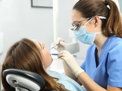 A dental hygienist assisting a patient in a dental clinic, with both wearing protective face masks and the patient seated in a dentist s chair.