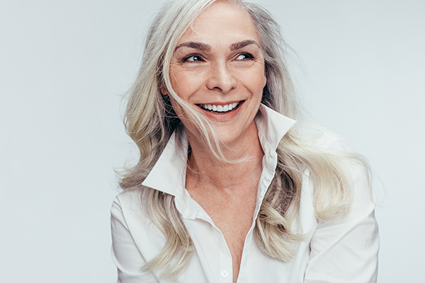 A smiling middle-aged woman with short hair, wearing a white top and leaning slightly forward.