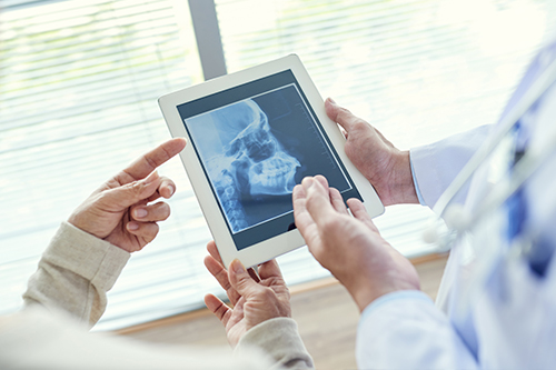 A tablet displaying a medical image being held by two people, with a third person holding a tablet showing the same image, all within a healthcare setting.