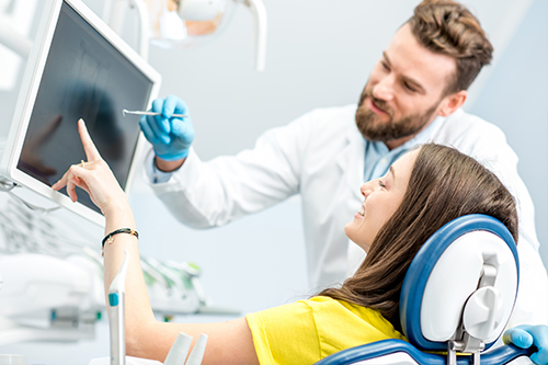An adult female patient is seated in a dental chair with a man standing next to her, both are in a modern dental office setting.