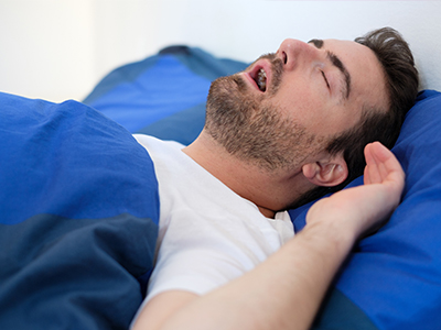 A man sleeping in bed with a blue comforter.