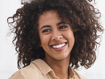 The image shows a smiling woman with curly hair, wearing what appears to be a brown top and a warm expression.